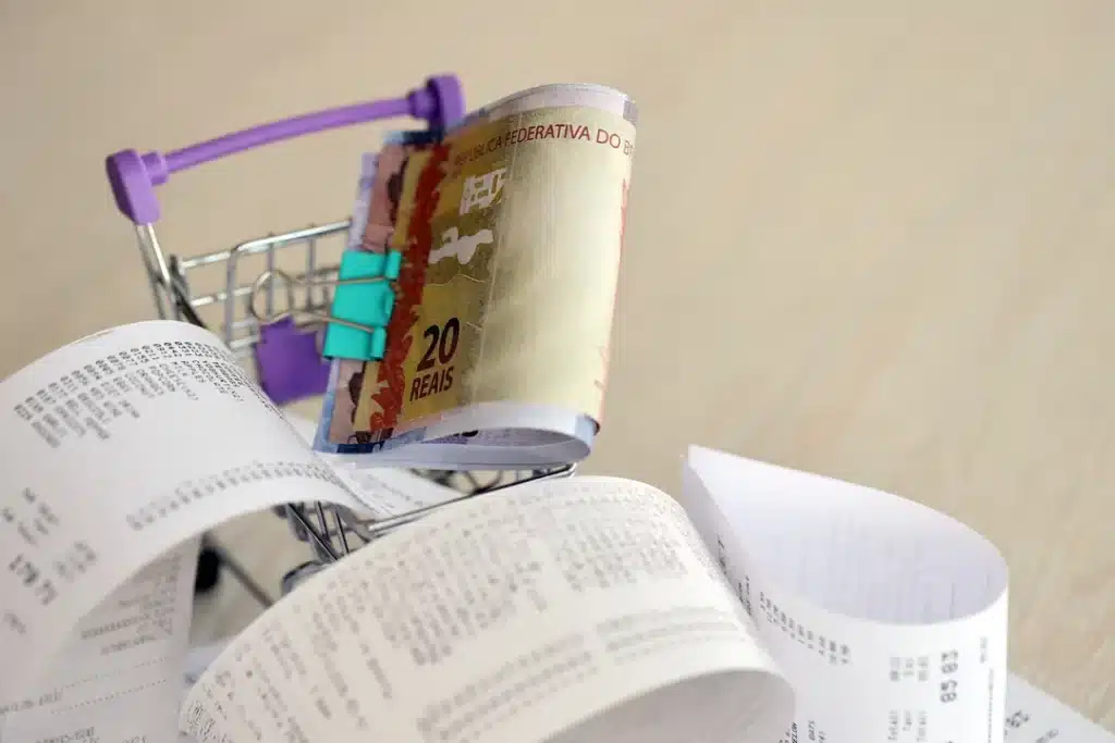 A miniature shopping cart filled with brazilian real cash and a long receipt, symbolizing financial transactions and compliance with brazilian accounting standards for accurate reporting and tax management.