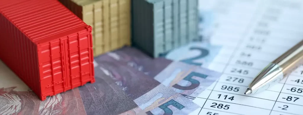 Miniature shipping containers placed on banknotes and financial documents, symbolizing customs and tax management handled by a customs broker in Brazil.